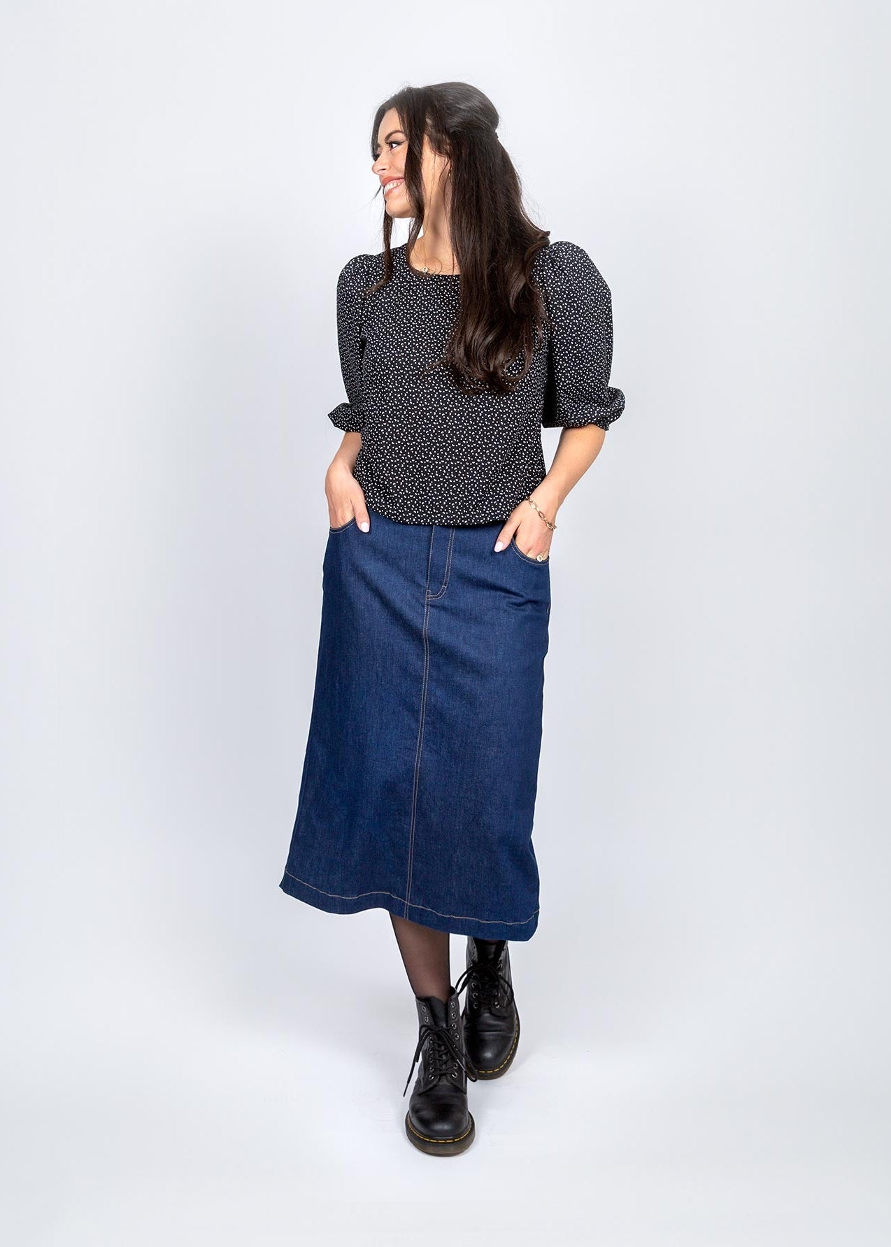 Woman wearing a black patterned top and blue denim skirt on a white background
